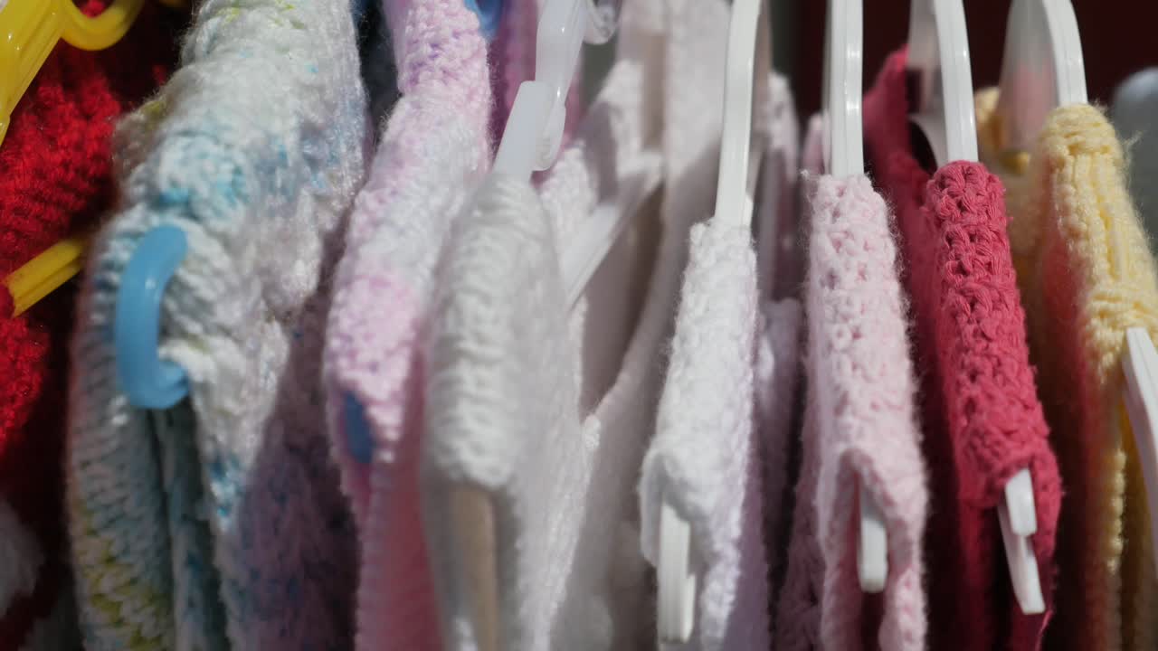 Colorful knitted baby clothes hanging on hangers
