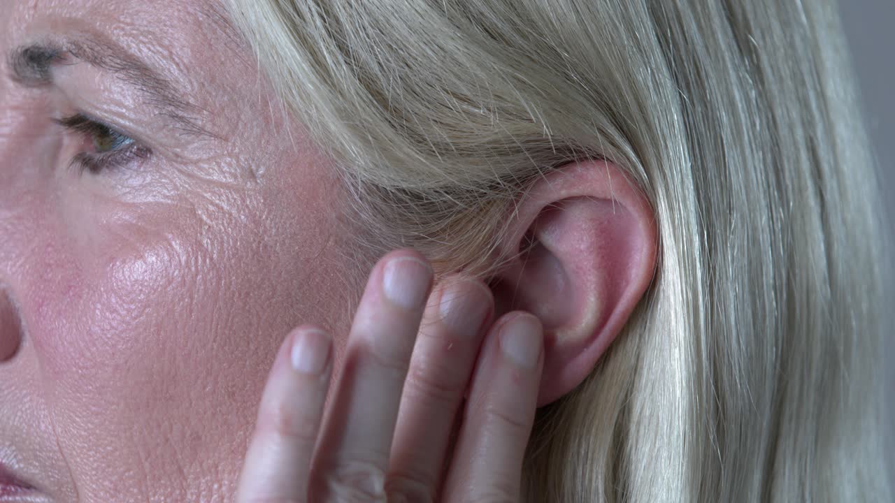 mujer que sufre tinnitus, frotando el oído sonoro