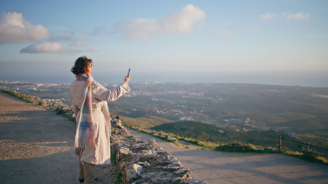 una mujer viajera tomando una selfie en su teléfono inteligente con la vibrante costa del atardecer.