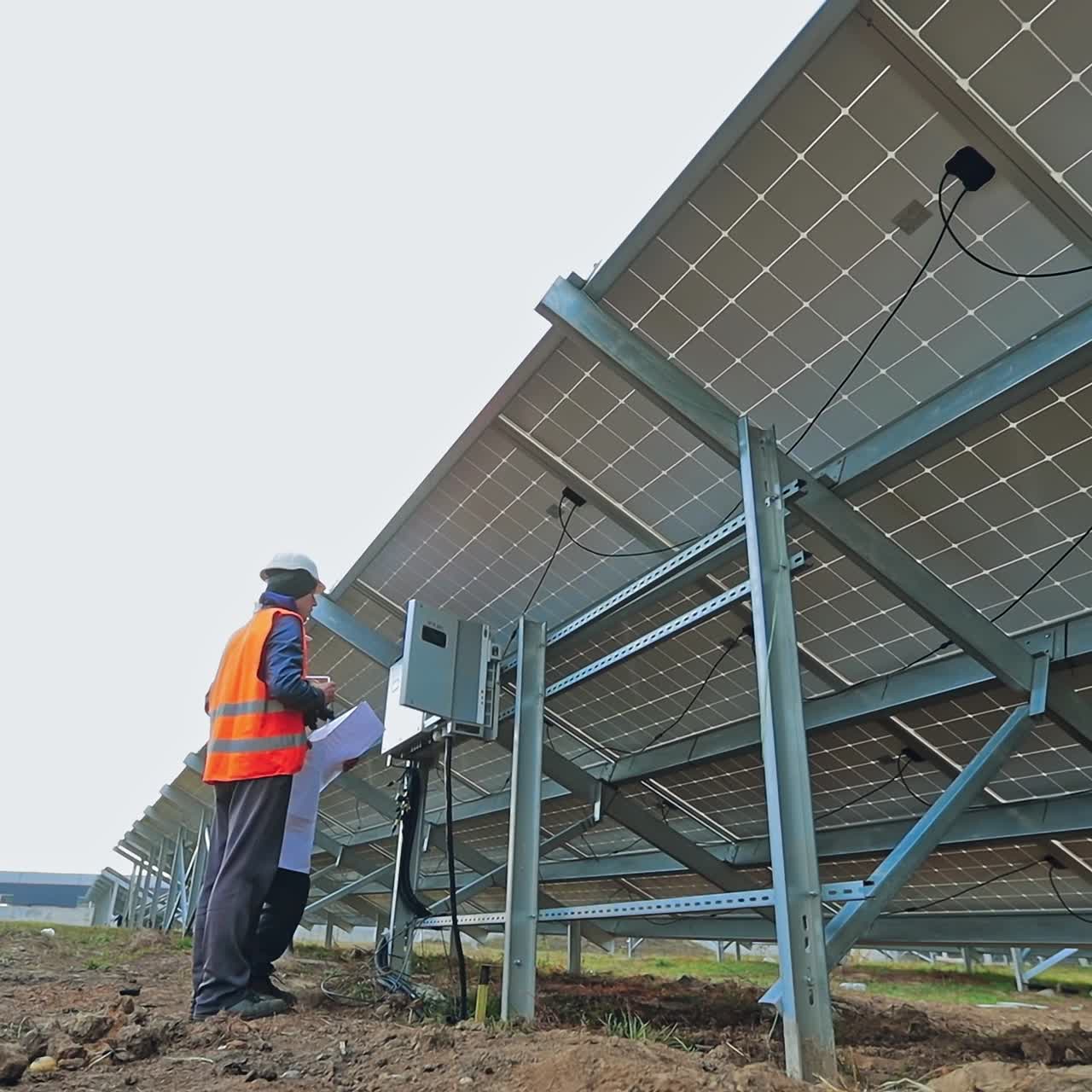 Installing solar panel. Man technician in special uniform connects the photovoltaic panel. View from below on a sunny battery.