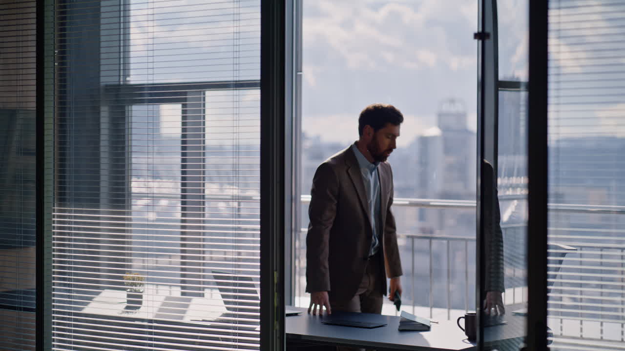 Manager furioso al telefono che gesticola emotivamente di fronte alla vetrata panoramica dell'ufficio