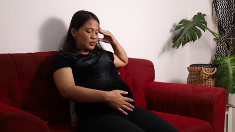 asian pregnant woman having headache while stroking the stomach at home