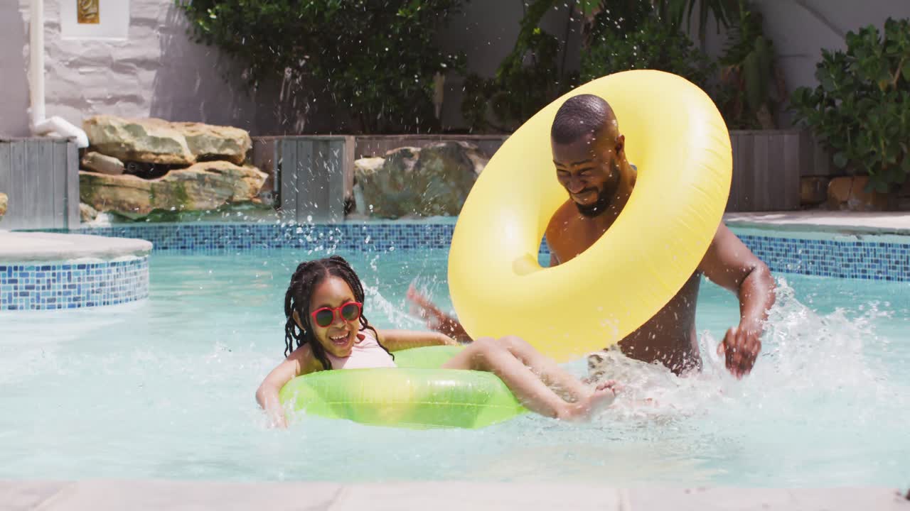 padre y hija afroamericanos felices divirtiéndose en la piscina con anillos inflables