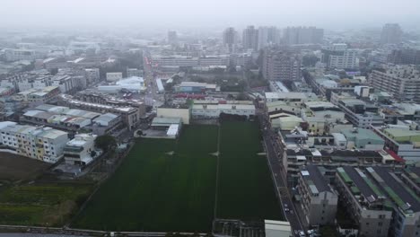 a sprawling urban area with buildings and a central green field on an overcast day, misty ambiance, aerial view