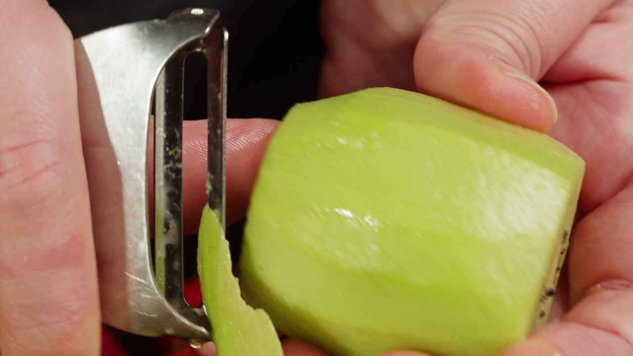 Hands Peeling a Fresh Kiwi with a Vegetable Peeler