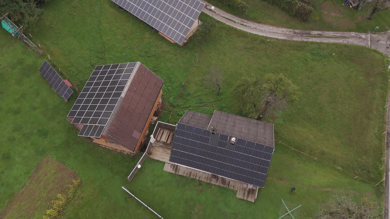 Luftoptagelse i stigende højde afslører huse på landet med store solpaneler på taget ved siden af en nærliggende solcellepark, der viser bæredygtig og grøn levevis