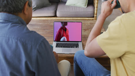 padre y hijo biraciales viendo la computadora portátil con un jugador de rugby afroamericano con la pelota en la pantalla