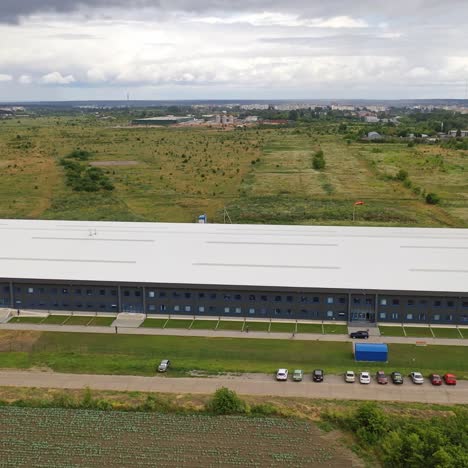 aerial panorama of a modern plant. exterior of a large commercial warehouse situated among green fields. camera moves forward.
