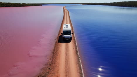 van driving on a road between a pink lake and a blue lake