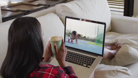 compuesto de una mujer sentada en casa sosteniendo un café viendo un evento de atletismo en una computadora portátil