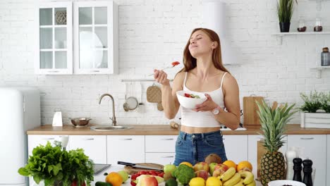 happy girl in the kitchen eats fresh vegetable salad from a plate. a table with vegetables and fruits for vegetarian food