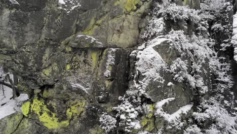 Levantando-Una-Formación-De-Piedra-Cubierta-De-Musgo-Mientras-La-Nieve-Cae-Suavemente,-Rocher-De-Bilisse,-Cierre-Aéreo