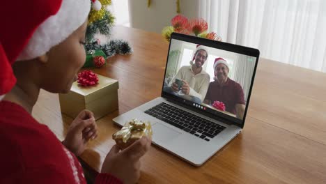 Mujer-Afroamericana-Con-Gorro-De-Papá-Noel-Usando-Una-Computadora-Portátil-Para-Una-Videollamada-Navideña,-Con-La-Familia-En-La-Pantalla