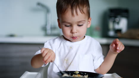 cute baby boy in white t-shirt and spots on it. adorable kid eating soup from big bowl. close up. blurred backdrop.