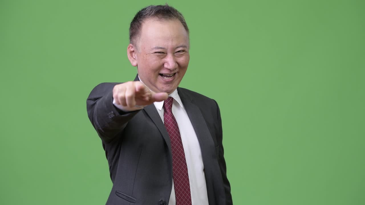 성숙하고 행복한 일본인 사업가가 카메라를 가리키고 있다.