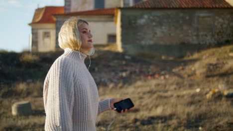 Señora-Tranquila-Caminando-Con-Auriculares-En-Los-Paisajes-Del-Castillo.-Mujer-Rubia-Escuchando-Música