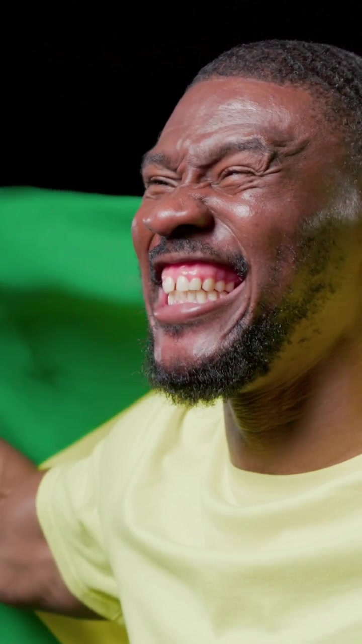 Video verticale: Uomo sorridente che festeggia in studio, avvolto nella bandiera brasiliana, maglietta gialla, spazio per il testo.