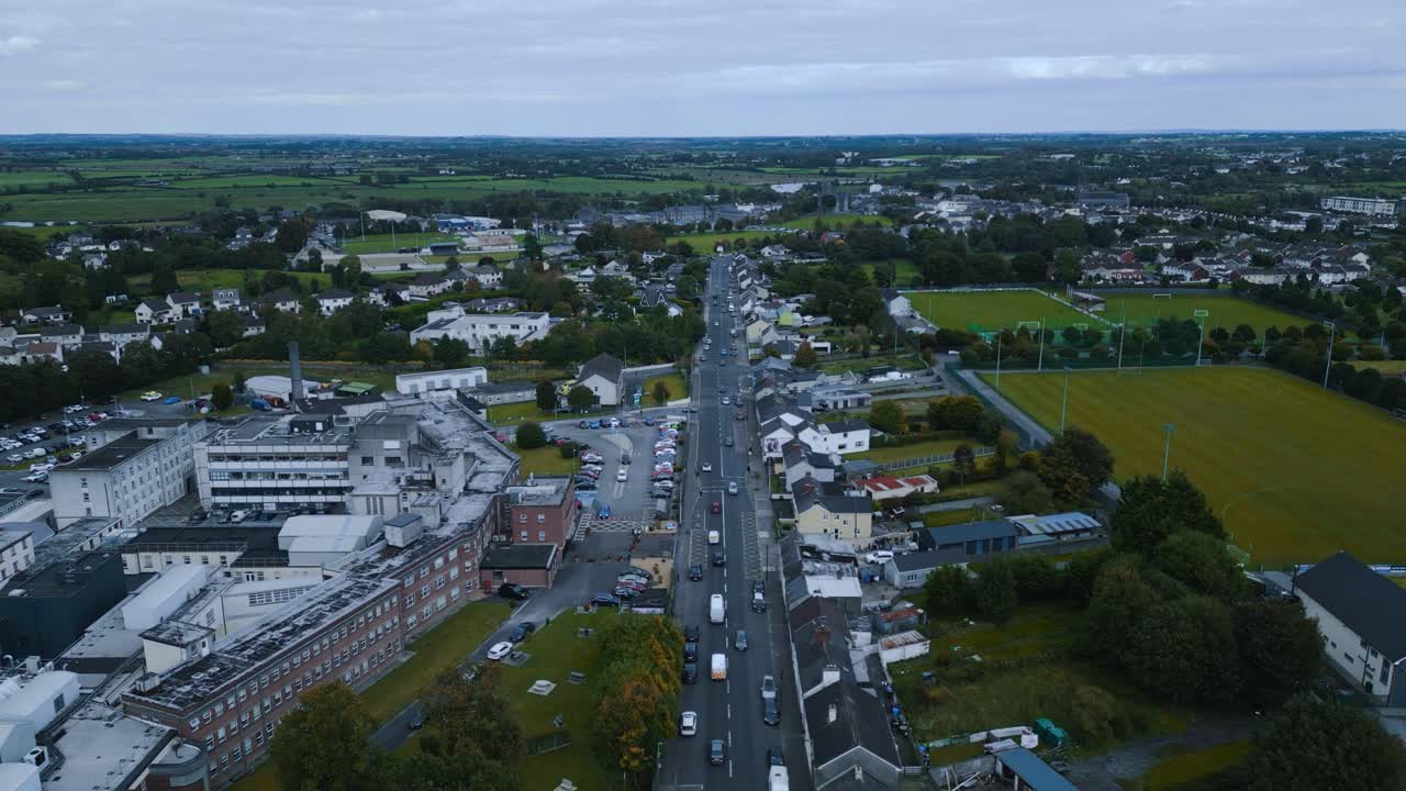 Cinematic drone footage pulling back over Ballinasloe, Ireland. Reveals the town's unique layout, from its dense center and hospital buildings to its peripheral sports fields and farms