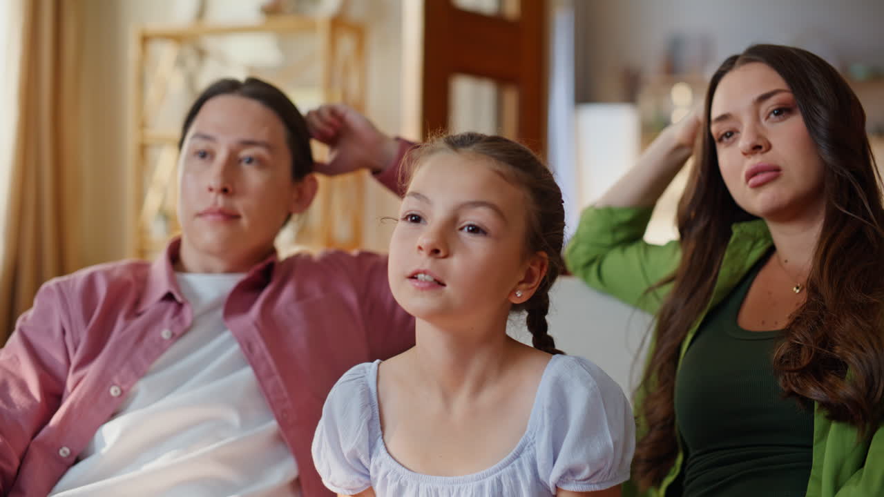 Bambino piccolo che tiene in mano un telecomando, primo piano sul divano. Famiglia che guarda un film