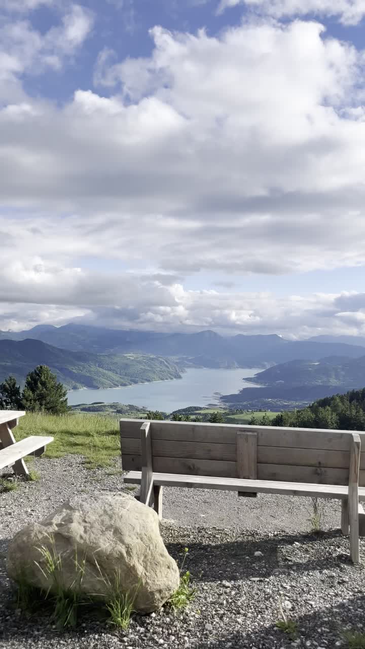 Vertical driving view over Lac de Serre-Ponçon, France. Scenic alpine lake, lush greenery, and dramatic clouds. Perfect for travel, road trip, and nature themes.