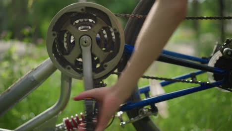 close-up of hand rotating bicycle pedal backward, causing the wheel to spin rapidly, the focus is on the gear system and chain, with the background featuring blurred greenery