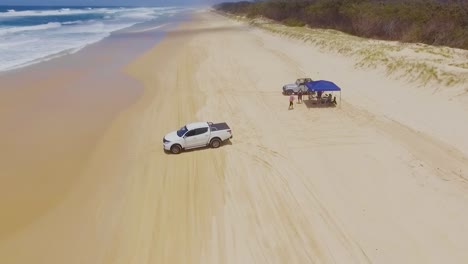 low aerial drone shot travelling south down main beach on queensland's north stradbroke island towards a camp site, with 4x4 four wheel drive vehicles driving on the beach