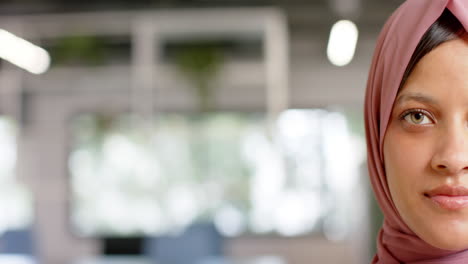 Half-portrait-of-happy-biracial-casual-businesswoman-in-hijab-in-office-with-copy-space,-slow-motion