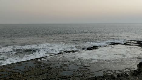 White-foamy-sea-wave-water-crashing-rocky-shore,-evening