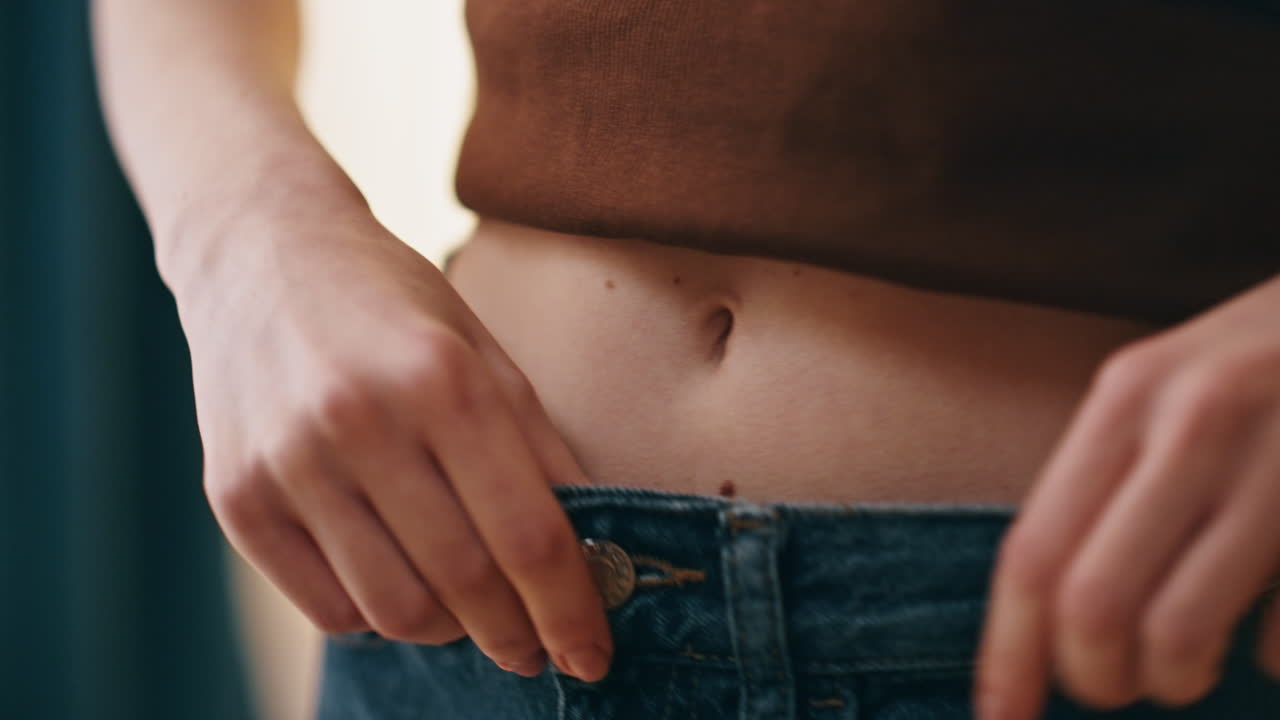 Hands fastening jeans button closeup. Woman checking waist weight loss progress