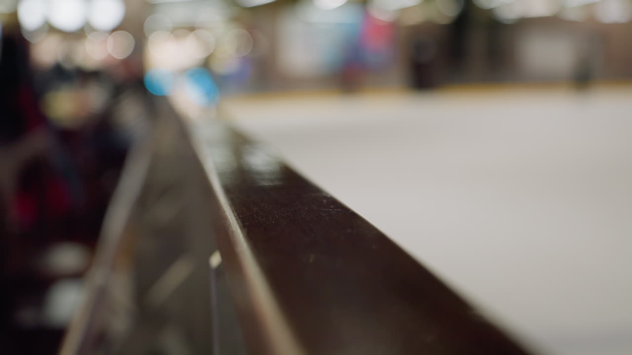 una vista sfocata di una zona sciistica con qualcuno che scia sullo sfondo, enfatizzando la ringhiera lucidata in primo piano e l'ambiente attivo della zona sciistica