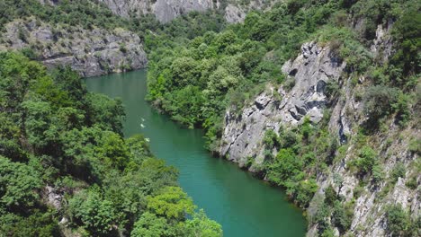 Aerial-view-of-three-kayaks-navigating-a-river-between-rock-canyons-and-forest-at-day-time