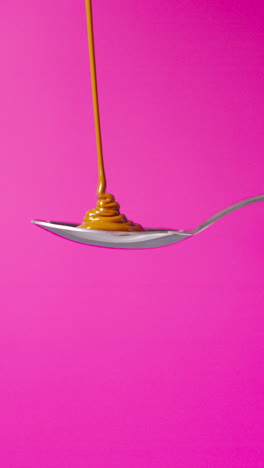 video vertical de chocolate derretido que se vierte en una cuchara y se desborda contra un fondo de color rosa con espacio de copia 1