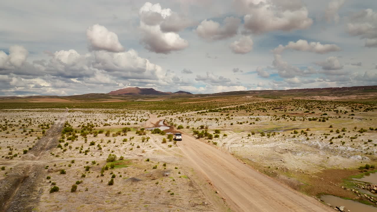 Vista aérea panorámica de una camioneta pick-up viajando por un camino de tierra a través del desierto de Siloli en Bolivia