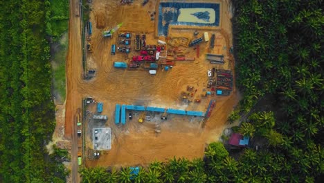 toma cinematográfica de drones de perforación en tierra y estructura de plataforma de reacondicionamiento y equipo de plataforma para exploración y explotación de petróleo en medio de la jungla rodeada de palmeras durante la puesta de sol