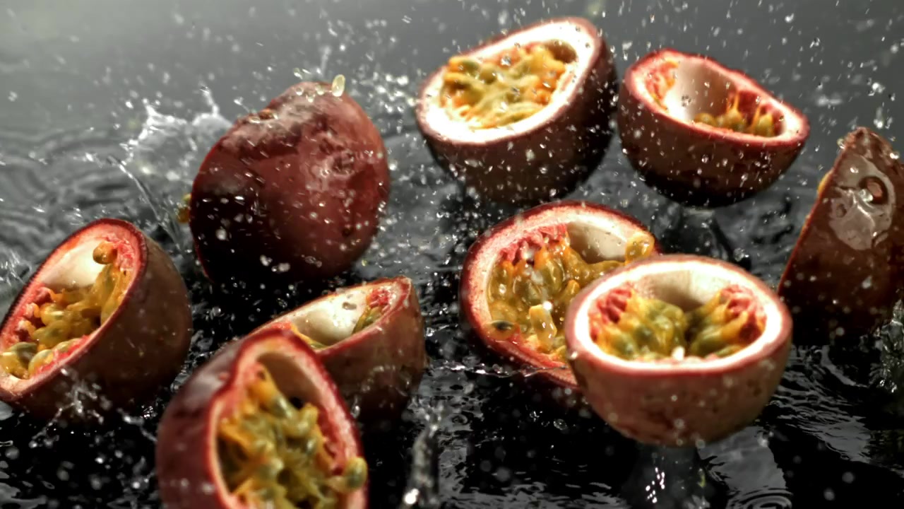 Friske halverede passionsfrugter plasker ned i vand i slowmotion