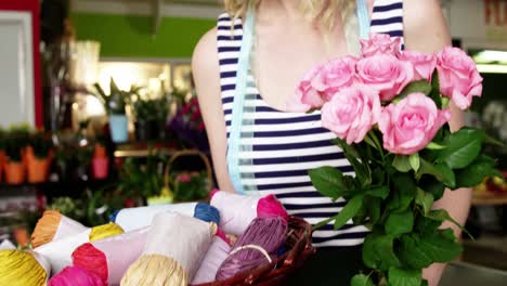 Female-florist-holding-a-bunch-of-pink-rose-and-twine-cord-in-flower-shop