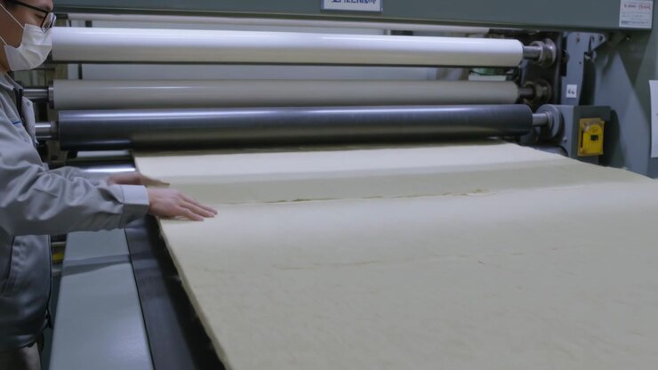 Guiding masked worker smoothing beige pad seam to keep aligned as machine feeding rollers at mill