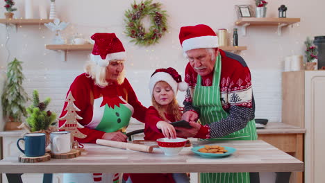 Senior-grandparents-and-grandchild-watching-cooking-lesson-using-digital-tablet-at-Christmas-kitchen