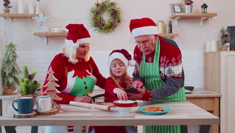 abuelos mayores y nietos viendo la lección de cocina usando una tableta digital en la cocina de navidad