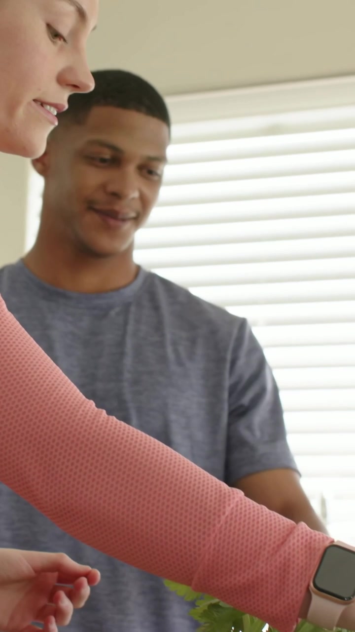 Vertical video: Reaching woman in pink cardigan making salad at kitchen counter man helping nearby