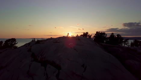 fly past inukshuk on rocky pine tree island at sunset, drone aerial wide dolly in