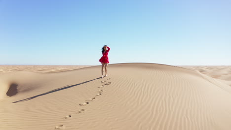toma cinematográfica de una mujer caminando por una duna de arena en el desierto, dejando huellas en la arena
