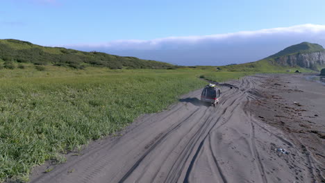 drone view follow black car driving on dusty road by the beach