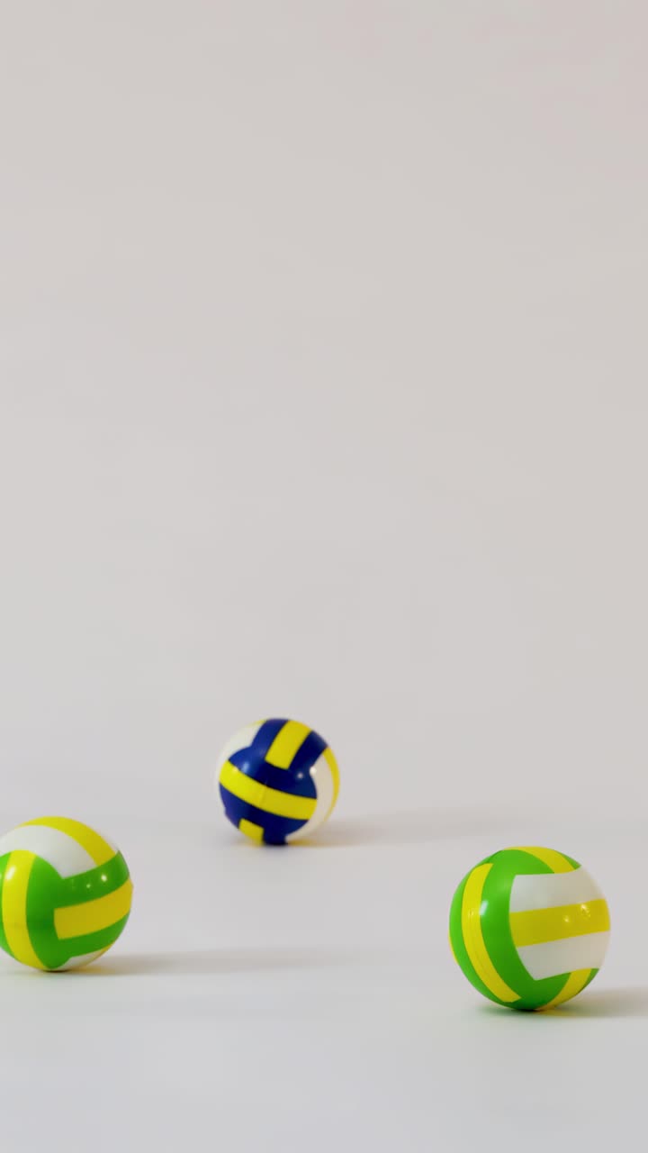 Small colorful volleyballs fall, bounce, and roll across a clean white studio floor surface