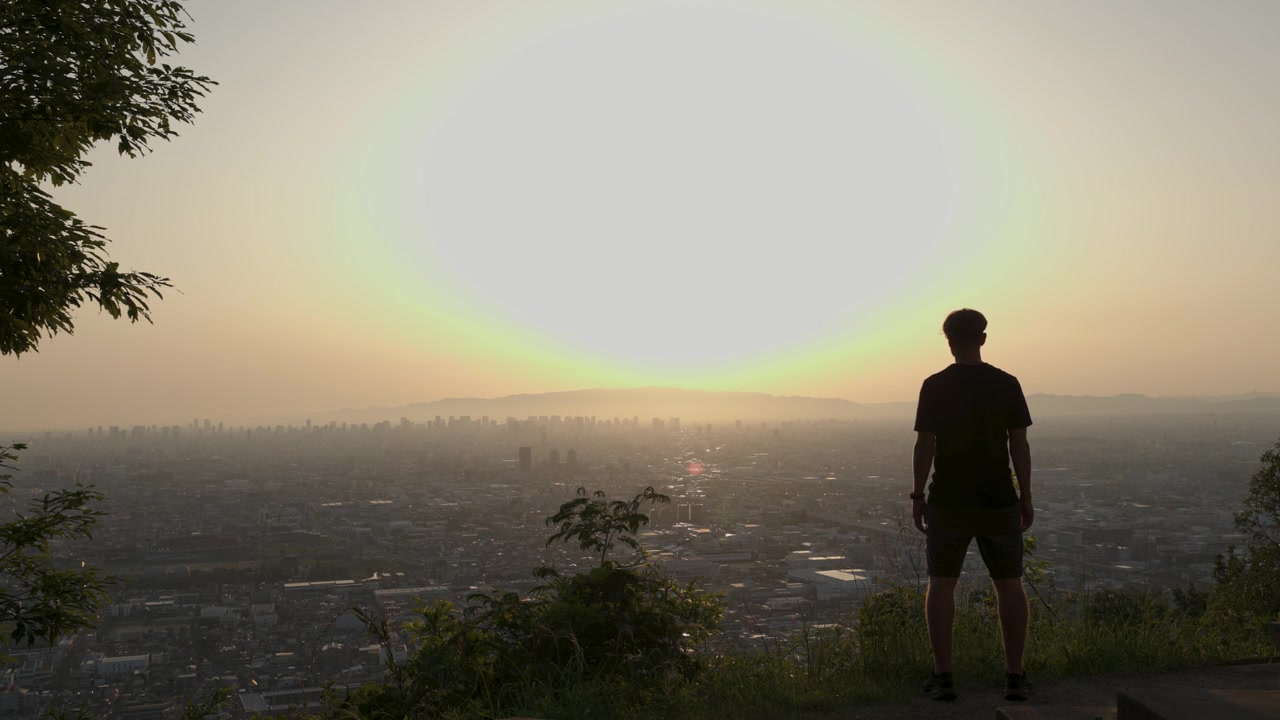 Uomo che osserva Osaka al tramonto da un punto panoramico lontano dalla città.