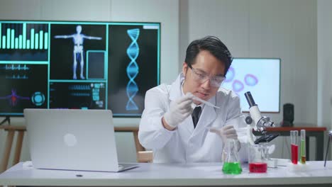 asian scientist man taking solution from test tube with micropipette putting in petri dish and talking to camera