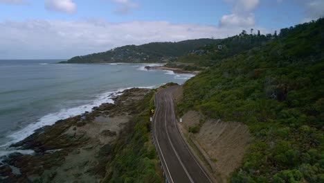 Great-Ocean-Road-reverse-aerial-shot-with-empty-highway-and-Wye-River-town-in-background,-Victoria,-Australia