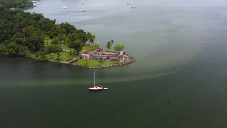 sailboat anchored off lush green tropical peninsula, aerial descend