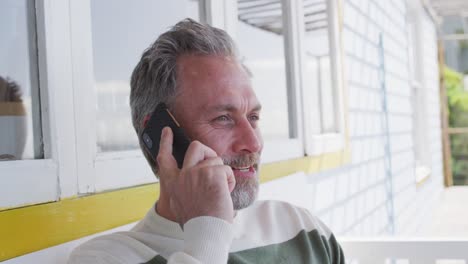 happy caucasian mature man siting on the terrace and using smartphone