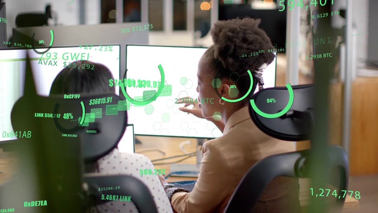 Tan blazer woman turning, pointing after colleague typing, reviewing green HUD finance on screens